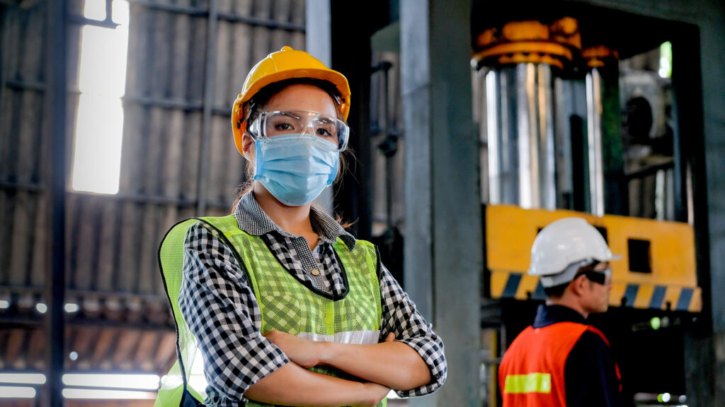 Factory woman worker wearing hygienic mask stand with confident action with her co-worker engineer in workplace during concern about covid pandemic in people affect industrial business.