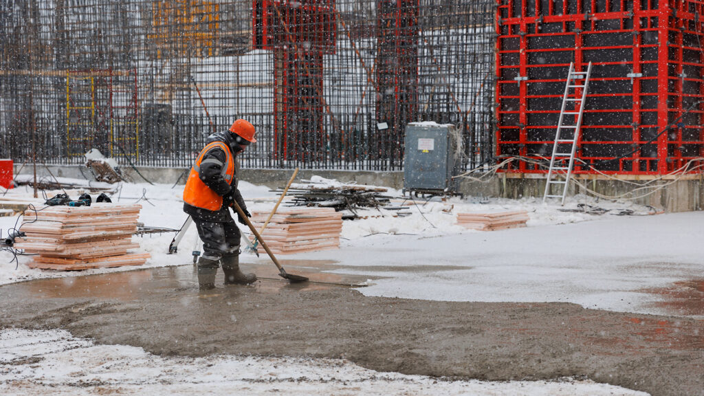 Construction worker leveling concrete at a construction site in a snowstorm