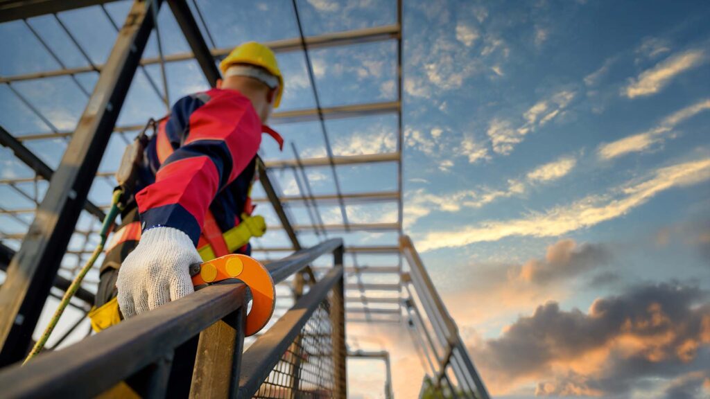 Close up of construction worker working at high heights clipping his safety harness to the railing