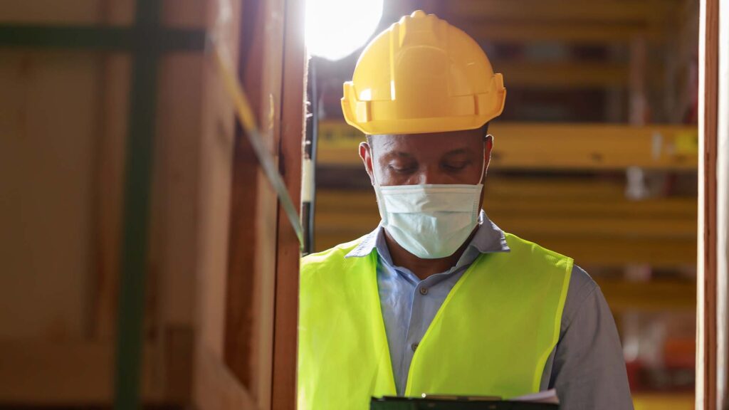Close up of a worker wearing face mask, safety vest, and hard hat in a warehouse facility